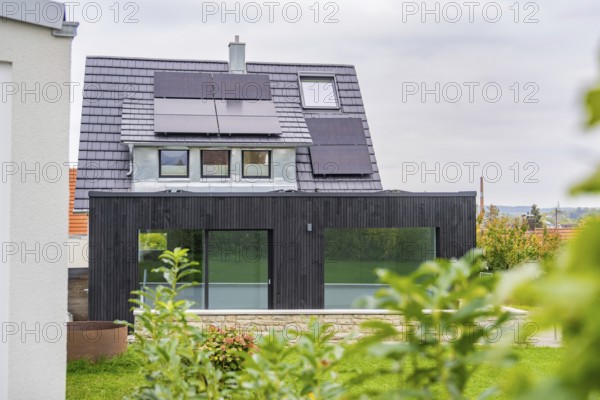 Modern house extension with glass front and solar panels, framed by plants in the foreground, quiet garden atmosphere in cloudy skies, house renovation, air conditioning renovation, Metzingen, Germany