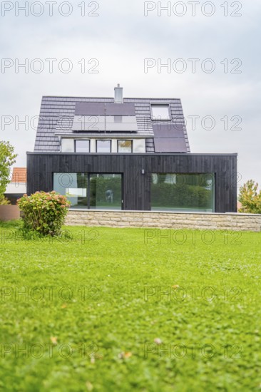 Single-family house with solar panels and black glass-fronted extension, large lawn in the foreground, quiet residential area with overcast sky, house renovation, air-conditioning renovation, Metzingen, Germany