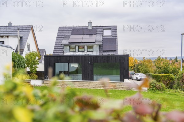 House with solar panels and black extension, view over garden to quiet street with parked car, house renovation, air conditioning renovation, Metzingen, Germany