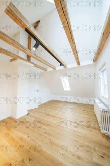 Light-flooded room under the roof with warm wooden floors and visible beam ceiling, house renovation, climate renovation, Metzingen, Germany