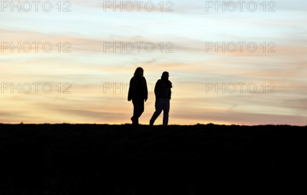 Walkers walk across a dike at sunset, Fehmarn Island, 13.10.2025, Fehmarn, Schleswig-Holstein, Germany