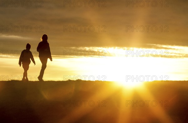 Woman and child walk across a dike on the island of Fehmarn at sunset, 13.10.2025, Fehmarn, Schleswig-Holstein, Germany