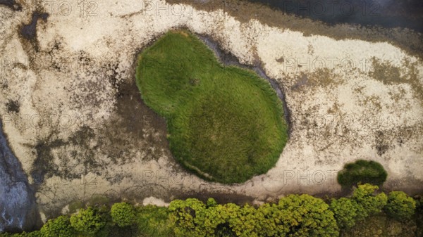 A patch of grass next to a calm dark lake on a cloudy day, seen from above