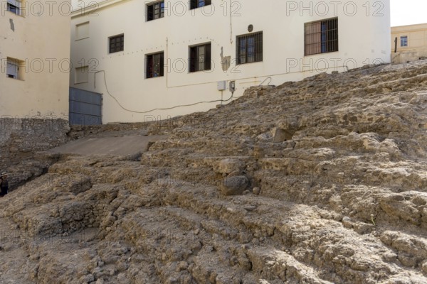 An old historic theatre in the middle of a town surrounded by houses. This landmark was photographed during the day. Teatro Romano de Cádiz, Andalusia, Spain