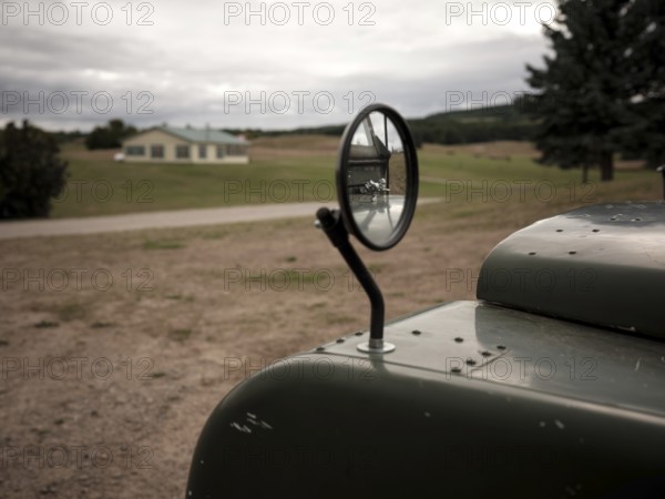 A cracked review mirror reflects a hood ornament on a 1950's Series One Land Rover on August 8, 2025 in Mulmer, Ontario, Canada