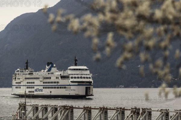 A large ferry on a calm body of water with mountains in the background under a cloudy sky in Horseshoe Bay, West Vancouver, British Columbia, Canada