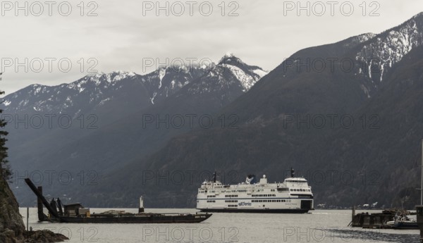 A ferry cruises through a scenic region with snowy mountains and cloudy skies in Horseshoe Bay, West Vancouver, British Columbia, Canada