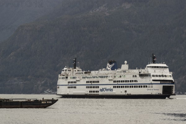 Ferry navigating across water with towering mountains under overcast skies in Horseshoe Bay, West Vancouver, British Columbia, Canada