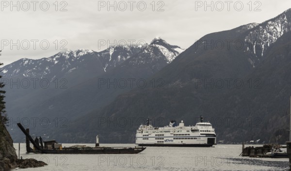 A ferry sails through calm waters with snow-capped mountains in the background in Horseshoe Bay, West Vancouver, British Columbia, Canada