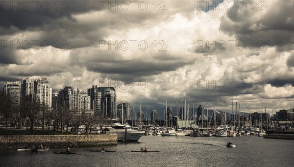 A vibrant cityscape with boats in the harbor beneath dramatic clouds in Vancouver, British Columbia, Canada