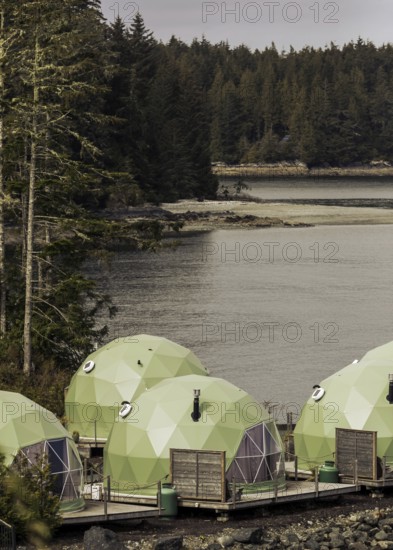 Green dome structures situated by the water with a forest backdrop in Tofino, British Columbia, Canada