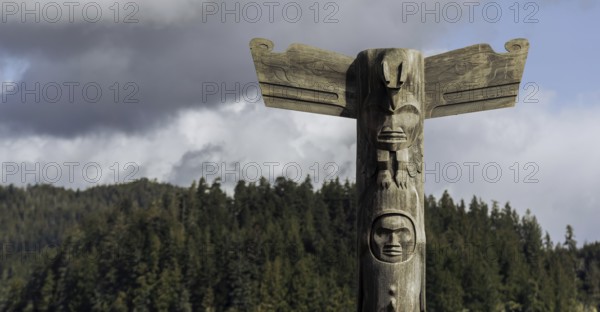 A totem pole set against a background of trees and cloudy sky in Tofino, British Columbia, Canada