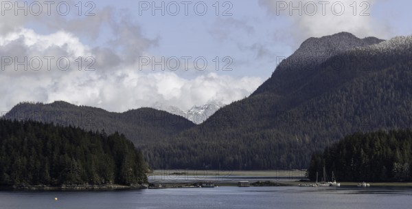 An expansive view of a lake bordered by forests and mountains under a cloudy sky in Tofino, British Columbia, Canada