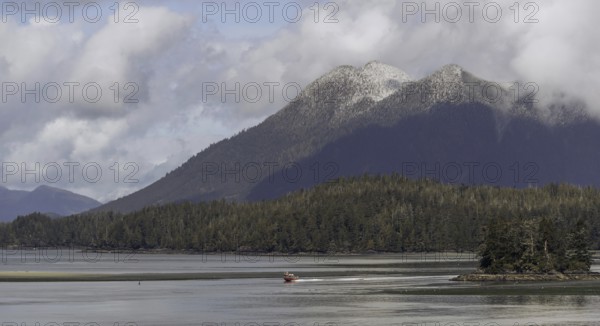 A small boat crosses a wide expanse of water with a backdrop of distant mountains and clouds in Tofino, British Columbia, Canada