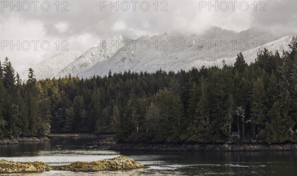 A serene waterway winds through a forest with snow-dusted mountains towering in the background in Tofino, British Columbia, Canada