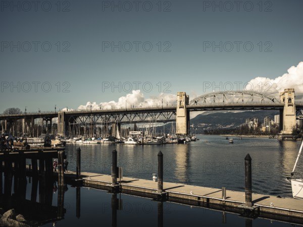 A wide bridge spans over a marina filled with boats, calm waters below in Vancouver, British Columbia, Canada