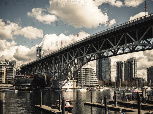 A grand bridge stretches over a busy harbor against a backdrop of clouds in Vancouver, British Columbia, Canada