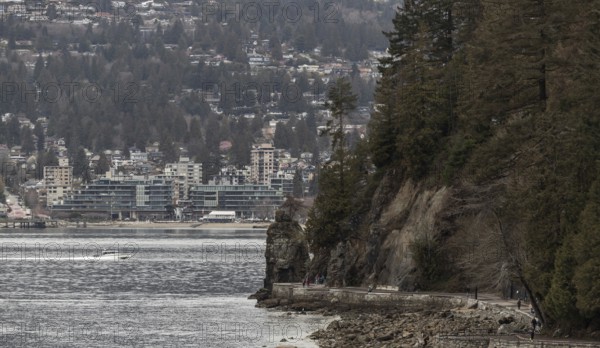 A rocky coastal path in Stanley Park with buildings and trees set against cloudy skies in Vancouver, British Columbia, Canada