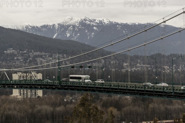 Suspension bridge with traffic, framed by an urban cityscape and mountain backdrop in Vancouver, British Columbia, Canada