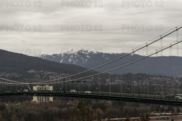 Suspension bridge spanning a city and mountainous landscape under cloudy skies in Vancouver, British Columbia, Canada