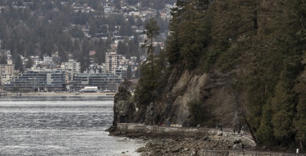 Rocks and trees line a coastal path in Stanley Park with urban buildings in the distance in Vancouver, British Columbia, Canada