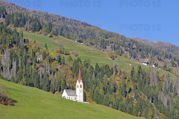 Lonely church with red tower on green alpine slope under bright blue sky, Dolomites, Drau cycle path, Tyrol, Italy
