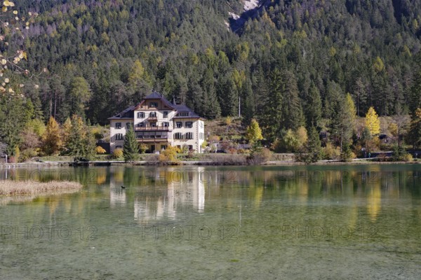 The villa is brilliantly reflected in a quiet alpine lake in front of dense forest and gentle slopes, Lake Toblach, Lake Dobbiaco, South Tyrol, Italy