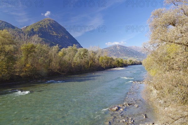 Clear river with gravel bank between autumn trees, mountains in the background under blue sky, Drava, Drau cycle path, Carinthia, Italy