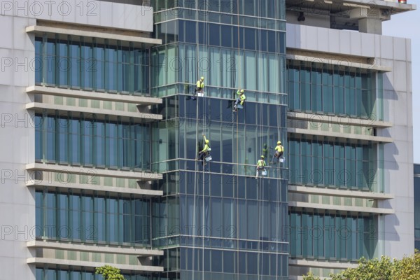 Window cleaners work as a team to clean the glass front of a hospital in downtown Bangkok, Thailand