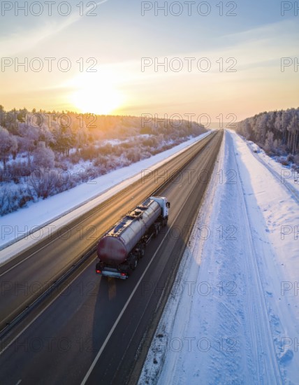 Petrol cargo truck lorry tanker driving on highway hauling oil products at sunrise, wide snowy landscape in winter, AI generated