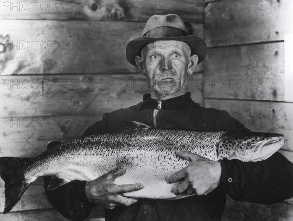 Fisherman with large salmon, presumably a king salmon or quinnat (Oncorhynchus tshawytscha), ca. 1930, USA