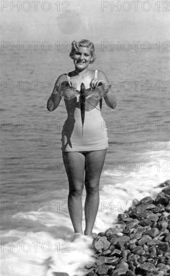 Woman on the beach in a bathing suit with flying fish, presumably swallowfish (Exocoetus volitans), 1940s USA