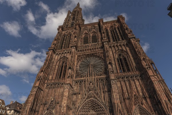 Strasbourg's Notre Dame Cathedral stands majestically there. Its magnificent architectural details are clearly visible under the blue, cloudy sky. Bas Rhin, Alsace, France