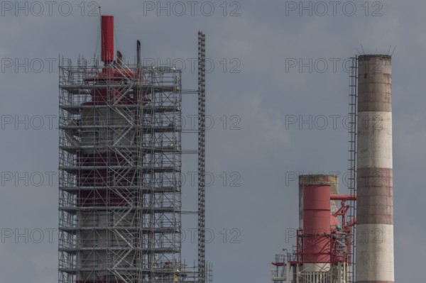 Workers work on a large chimney covered with scaffolding. Two chimneys are visible and the sky is cloudy. The activity takes place in a factory. Upper Rhine, Alsace, France