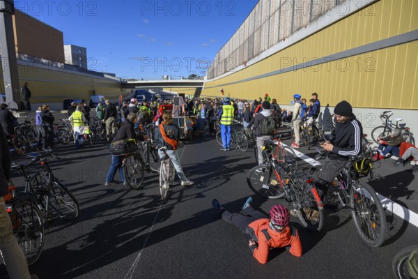 Cyclists wait to continue their journey. Meanwhile, a woman wearing a helmet is lying on the asphalt and resting. Bicycle demo on the recently inaugurated 16th construction phase of the A100, Berlin, 18.10.2025