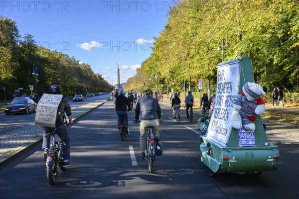 Participants in a bicycle demo against the A100 on the 17th of June road. Signs say: Hitler loves (heart) Autobahn, CDU continues the delusion #A100 and fair movement instead of laying concrete. A100 wegbassen, Victory Column, Berlin, 18.10.2025