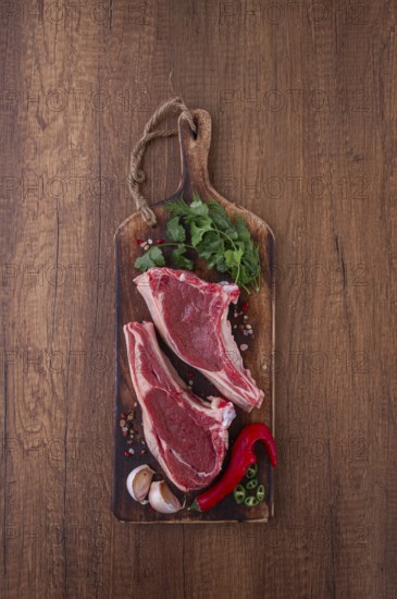 Freshly sliced lamb chops, with herbs and vegetables, on a wooden board, ready to cook, on a wooden table