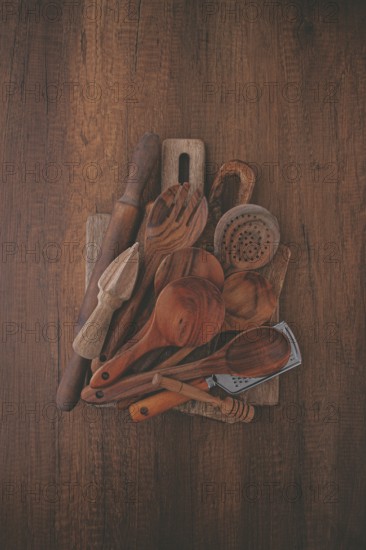 A variety of wooden kitchen utensils are arranged on a dark brown wooden surface. Items include spoons, a spatula, and a rolling pin, showcasing their unique textures and shapes