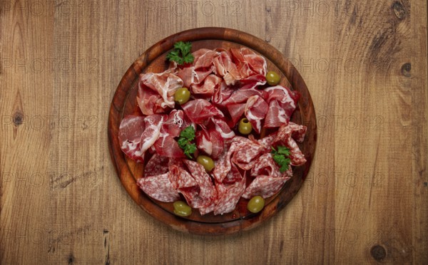 Assortment, sliced meat appetizer, prosciutto, salami and ham, with olives, on a wooden board, breakfast, top view, close-up, no people