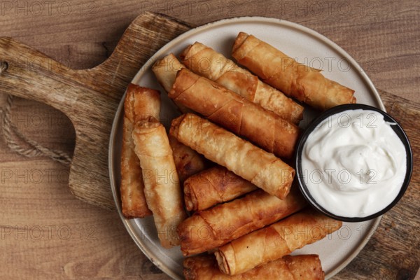 Fried spring rolls with cheese, on a wooden background, with cream sauce, no people