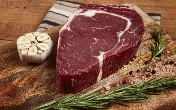 Raw steak, beef steak, rib eye steak, on a cutting board, freshly frozen, with spices and herbs, on the table, top view