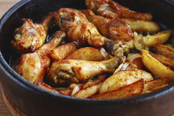 Fried chicken drumsticks with potato slices, in a clay pan, baked in the oven, with spices, homemade, no people