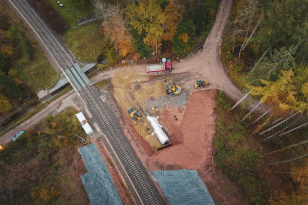 Construction site next to railway line with excavators and trucks surrounded by autumn forests, Hermann-Hesse-Bahn construction site, Calw, Germany