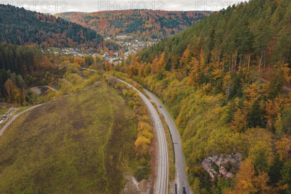 Winding road with rails through autumnal forest, village in the background, Hermann-Hesse-Bahn construction site, Calw, Germany