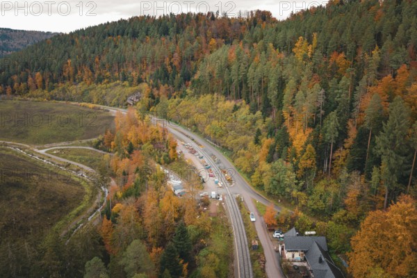 Road next to railroad tracks through autumnal forest and hills, Hermann-Hesse-Bahn construction site, Calw, Germany