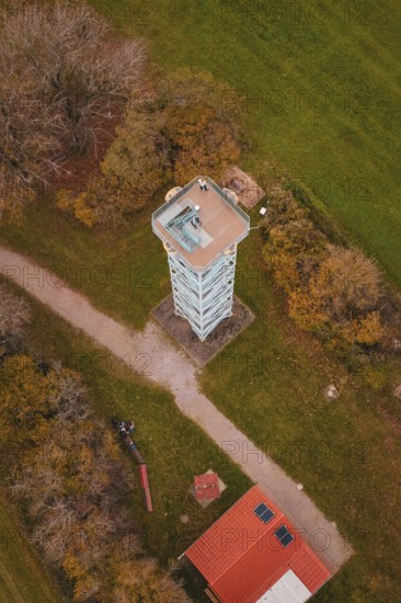 Aerial view of a tower surrounded by trees and paths in autumn colors and green fields, Dürrenmettstetten observation tower, Germany