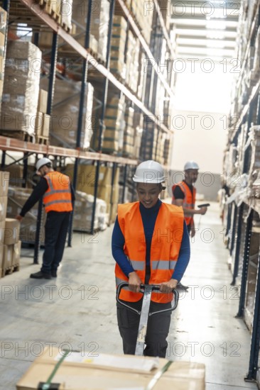 Diverse logistics team preparing packages and moving products on pallet jacks inside a modern distribution warehouse with racks of inventory and staff in safety vests and hard hats
