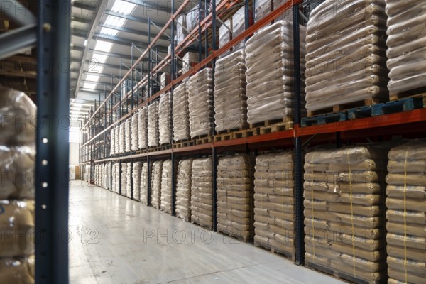 Spacious industrial warehouse aisle with pallets of identical sacks stacked on tall metal shelving, organized inventory showcasing efficient logistics and commercial distribution operations