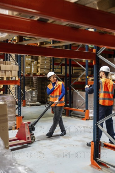 Diverse team of warehouse workers communicating while managing inventory and moving goods with a hand pallet truck among storage racks in a distribution center