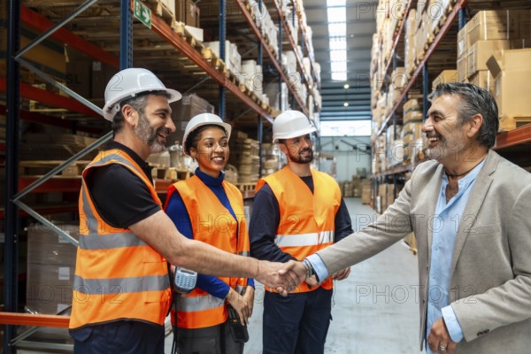 Diverse logistics team and supervisor standing in a distribution warehouse, a manager congratulating an employee and offering an agreement or collaboration